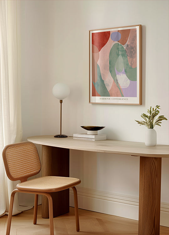 uno spazio di lavoro minimalista con una scrivania in legno, una sedia intrecciata, una lampada e un dipinto astratto incorniciato sul muro.