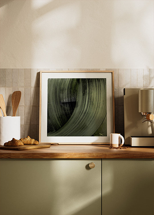 una fotografia incorniciata di una foglia verde sul bancone della cucina, con una caffettiera e altri oggetti da cucina visibili sullo sfondo.