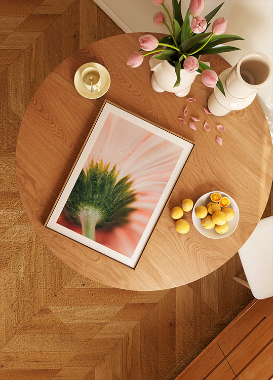 un tavolo di legno con l'immagine incorniciata di un fiore, una ciotola di frutta e un vaso di fiori rosa.