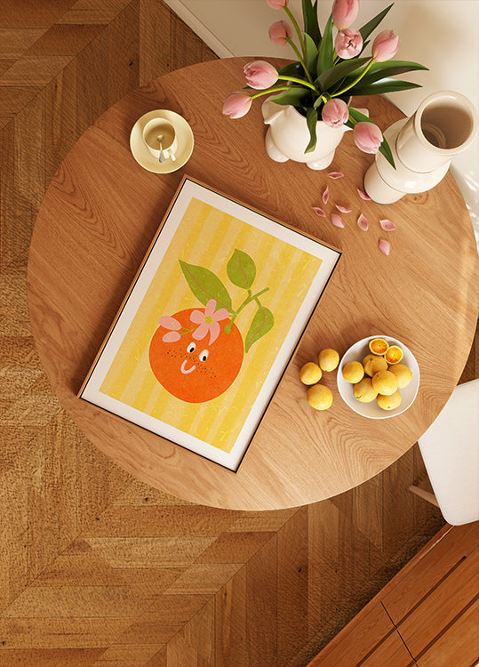 un tavolo di legno con l'immagine incorniciata di un'arancia, una ciotola di limoni, un vaso di tulipani rosa e una candela sopra.