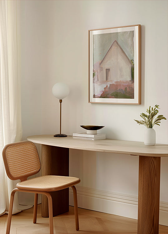 uno spazio di lavoro moderno e minimalista con una scrivania in legno, una sedia intrecciata, una lampada e un dipinto incorniciato di una casa.