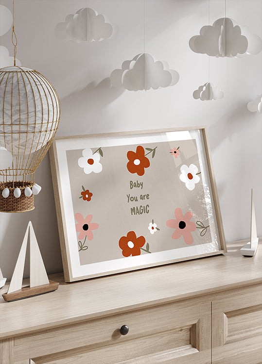 Una stampa incorniciata con un disegno floreale e il testo "Baby You are Magic" è esposta su un comò in legno, con una lanterna di carta decorativa appesa sopra di esso.